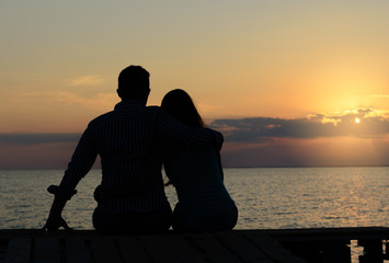 Two people in love (couple) sit on the bridge and admire the sunset. Weekend, vacation, honeymoon, romance.