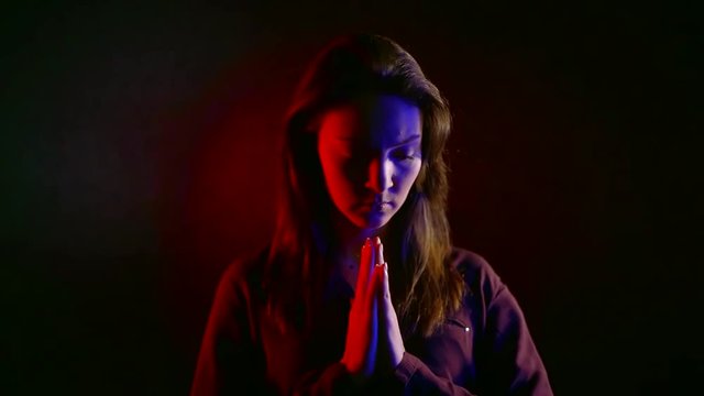 young sad woman praying in dark room in neon light red and blue