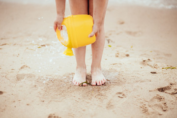 A child is playing on the beach. Water runs to the sand from the watering can.