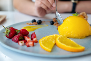 A woman eating orange cake with mixed fruit by spoon in cafe