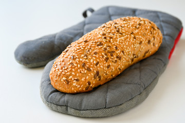 Freshly baked brown sesame loaf on a grey baking glove