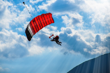 Paraglider with red parachute flying in the blue sky with white clouds on a sunny day