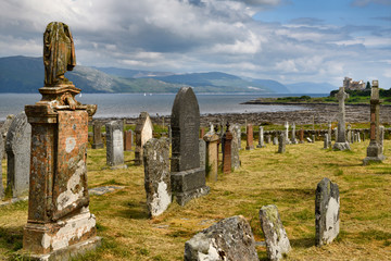 Ancient tombstones at Kilpatrick Cemetery next to Duart Castle on Isle of Mull with sailboats on Sound of Mull at Loch Linnhe Scotland UK