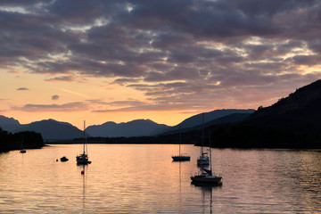 Moored sailboats on Loch Leven with red sky sunset clouds at Glencoe Boat Club and distant Sgurr Dhomhnuill peaks Scottish Highlands Scotland