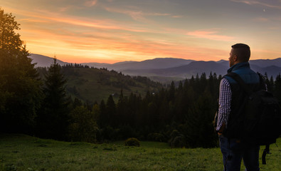 A bearded man (tourist) in a sleeveless jacket with a backpack stands on top of the hills and...