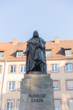 A close up of Albrecht Dürer statue in Nuremberg standing before living houses with blue sky above