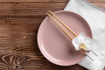 Plate with orchid flower and chopsticks on wooden background