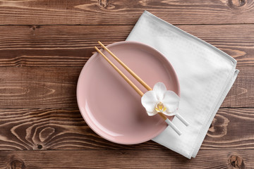 Plate with orchid flower and chopsticks on wooden background