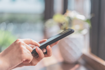 Close up woman hand using smart phone in cafe shop with bokeh light background.