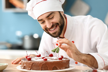 Male confectioner decorating tasty chocolate cake in kitchen - obrazy, fototapety, plakaty