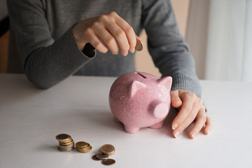 Woman putting money into piggy bank on table. Concept of savings