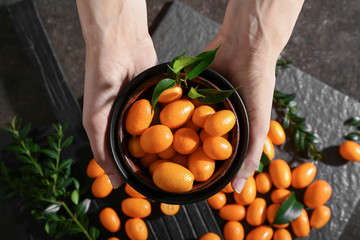 Female hands holding bowl with delicious kumquat fruit over table