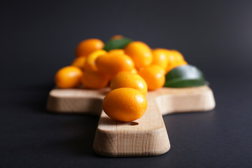 Board with delicious kumquat fruit on dark background