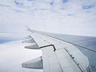 View from the window of a transatlantic airliner - the wing of an airplane above cumulus white clouds.