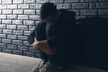 Depressed man thinking about suicide while sitting near dark brick wall