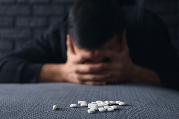 Heap of pills and depressed young man on background. Suicide awareness concept