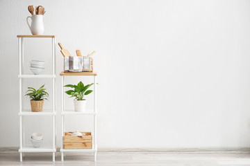 Shelves with kitchenware near white wall