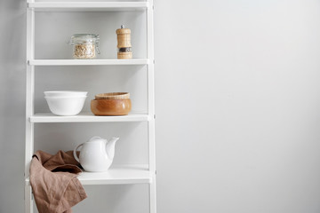 Fototapeta na wymiar Shelves with kitchenware near white wall