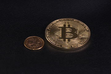 a small coin near a large coin bitcoin on black leather
