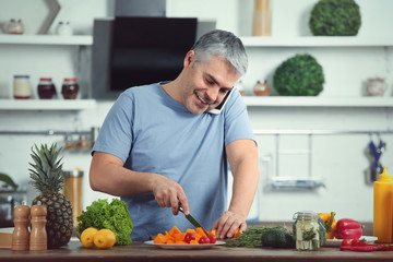 Mature man talking by phone while cooking dinner at home