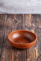 An empty plate of red clay stands on a wooden table, copy space