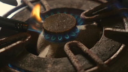 close up detail shot of old rusty kitchen stove ring switched on fire with lighter flame burning in dangerous gas energy and domestic cooking concept