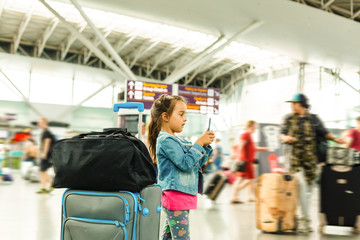 Little girl playing games on smartphone in airport departure area