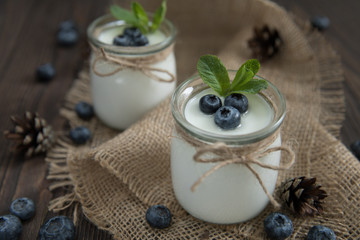 Fresh natural homemade organic yogurt with blueberries, in a glass jar on a wooden background