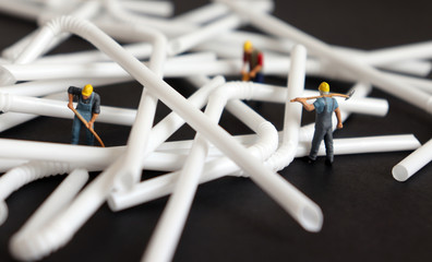 Miniature people with disposable plastic straws on the black background.