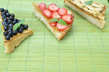 different delicious toasts on green or pink crimson background. Healthy sandwich for breakfast or snack. Toast with raspberries, strawberries, banana and blueberries and peanut butter. picnic concept