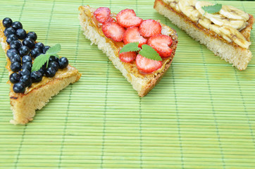 different delicious toasts on green or pink crimson background. Healthy sandwich for breakfast or snack. Toast with raspberries, strawberries, banana and blueberries and peanut butter. picnic concept