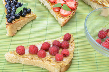 different delicious toasts on green or pink crimson background. Healthy sandwich for breakfast or snack. Toast with raspberries, strawberries, banana and blueberries and peanut butter. picnic concept