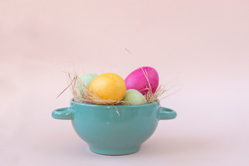 yellow, pink and green eggs in hay in a plate, beige background, Easter,