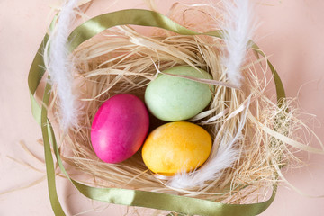 3 eggs, Easter, pink, yellow, green eggs in the nest, white feathers , green ribbon