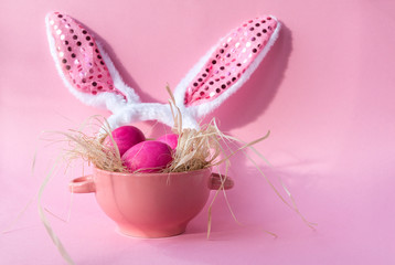 pink Easter eggs in hay in a plate, pink rabbit ears