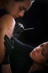 Female tattoo artist making tattoo on a men’s arm