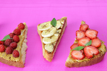 different delicious toasts on green or pink crimson background. Healthy sandwich for breakfast or snack. Toast with raspberries, strawberries, banana and blueberries and peanut butter. picnic concept
