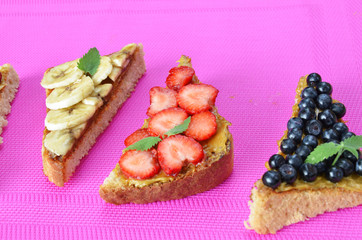 different delicious toasts on green or pink crimson background. Healthy sandwich for breakfast or snack. Toast with raspberries, strawberries, banana and blueberries and peanut butter. picnic concept