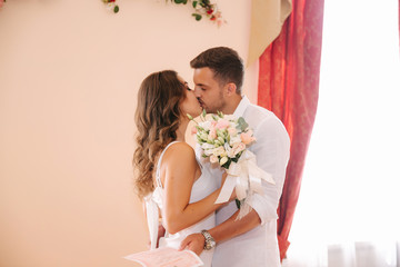 Kiss of beautiful couple. Groom in white shirt kiss his elegant bride in white dress. Bouquet of flowers in hands