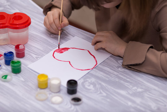 Child making homemade greeting card. Little girl paints heart on homemade greeting card as gift for Mother Day. Traditional play concept. Arts concept