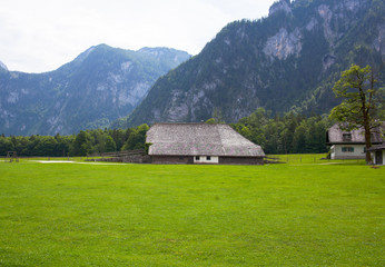Wooden house stands on a green lawn in the Alps