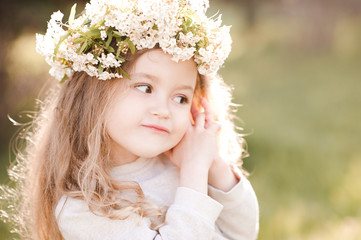 Funny baby girl 3-4 year old wearing flower wreath outdoors over green background. Childhood. Spring season.