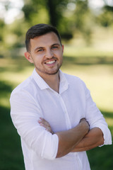Fototapeta premium Handsome man in a white shirt and shorts smile. Male model outside. Background of park. Young attractive man walking in the park
