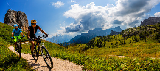 Fototapeta Cycling woman and man riding on bikes in Dolomites mountains landscape. Couple cycling MTB enduro trail track. Outdoor sport activity. obraz