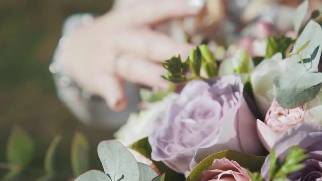 wedding festive preparation, charming bride tenderly strokes bouquet of purple pink white roses, girl shows elegant wedding ring with brilliant expensive stone, macro shoot, creative colors. no face