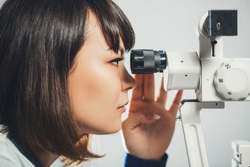 ophthalmologist Intern looks into eyepiece of eye-checking apparatus. Ophthalmology, hospital,...