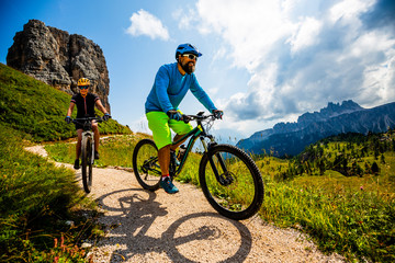 Cycling woman and man riding on bikes in Dolomites mountains landscape. Couple cycling MTB enduro...