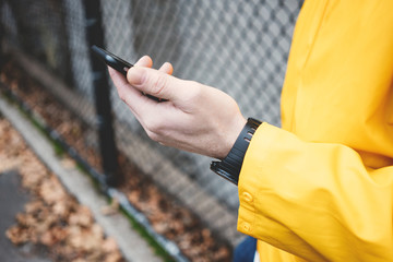 Close-up of mobile phone in hand. Man in yellow raincoat on the street