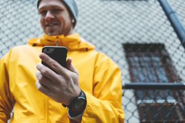 Man in yellow raincoat standing on the street with mobile phone and smartwatch