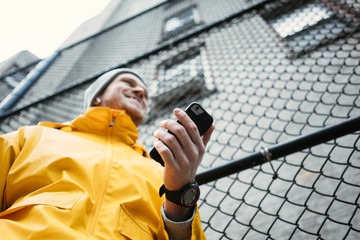Happy man in yellow raincoat standing on the street with mobile phone and smartwatch